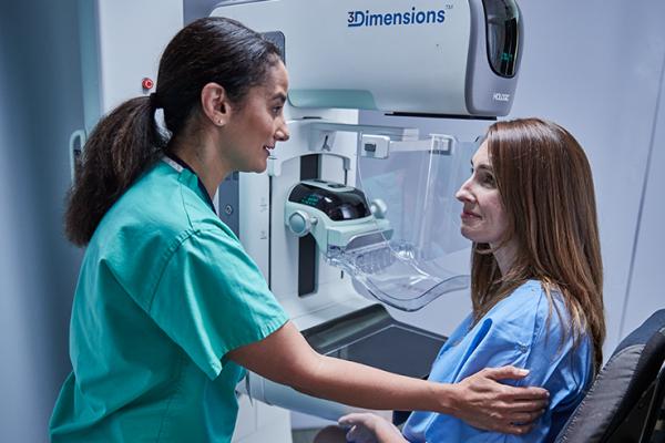 Donne sedute davanti a un mammografo a fianco di un operatore sanitario.