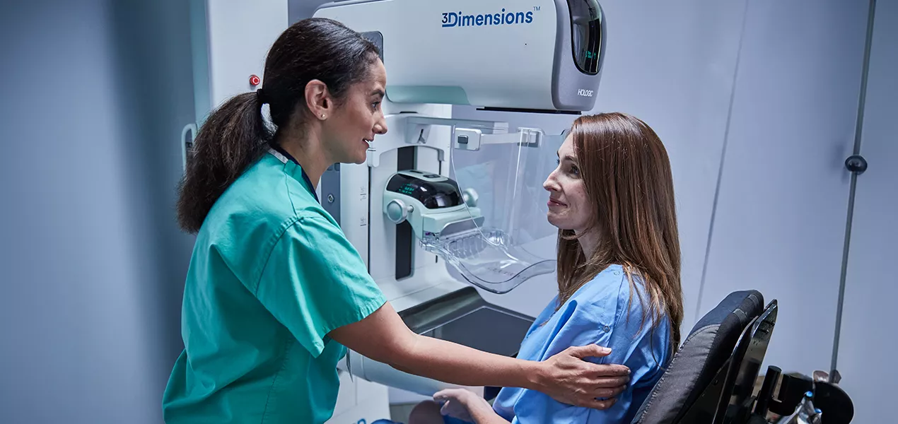 Donne sedute davanti a un mammografo a fianco di un operatore sanitario.
