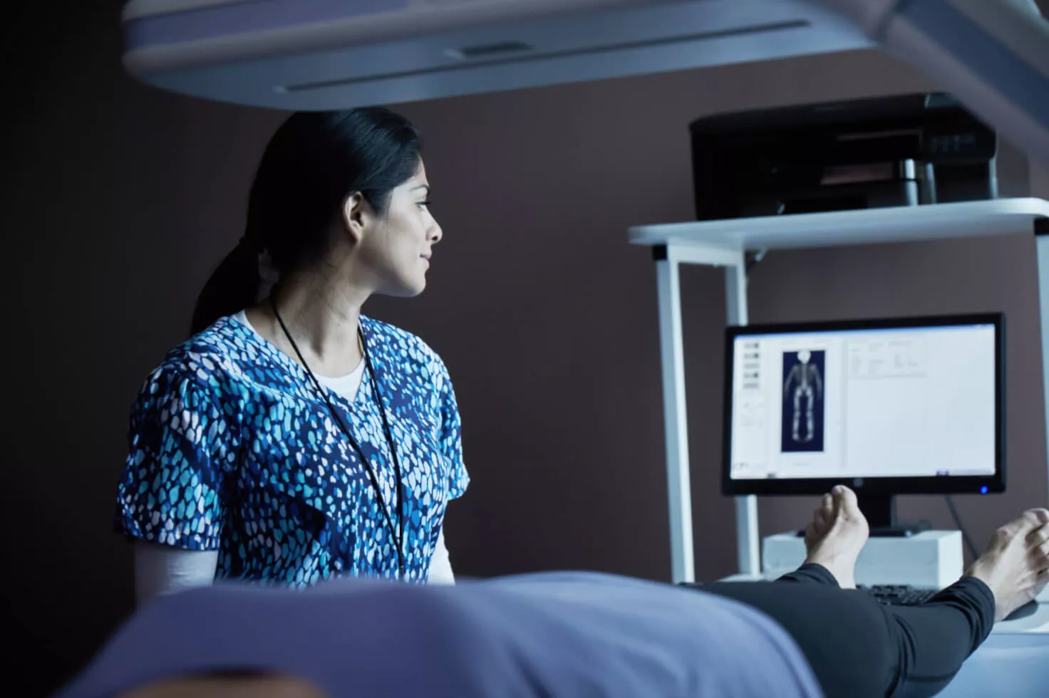 Operatore sanitario che osserva una scansione su un monitor con una paziente sdraiata a letto
